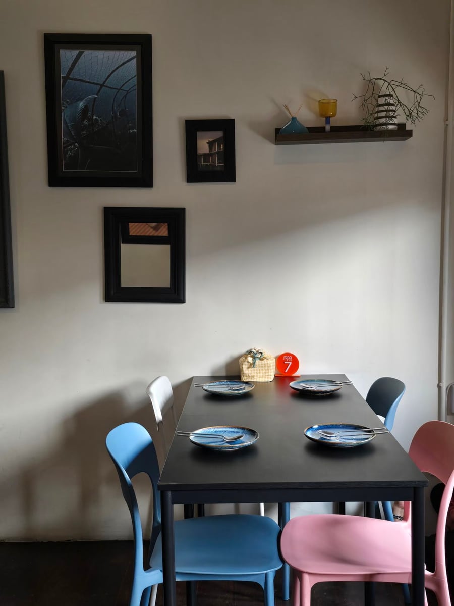 A corner table set for four beside the wall, under framed prints and a small shelf